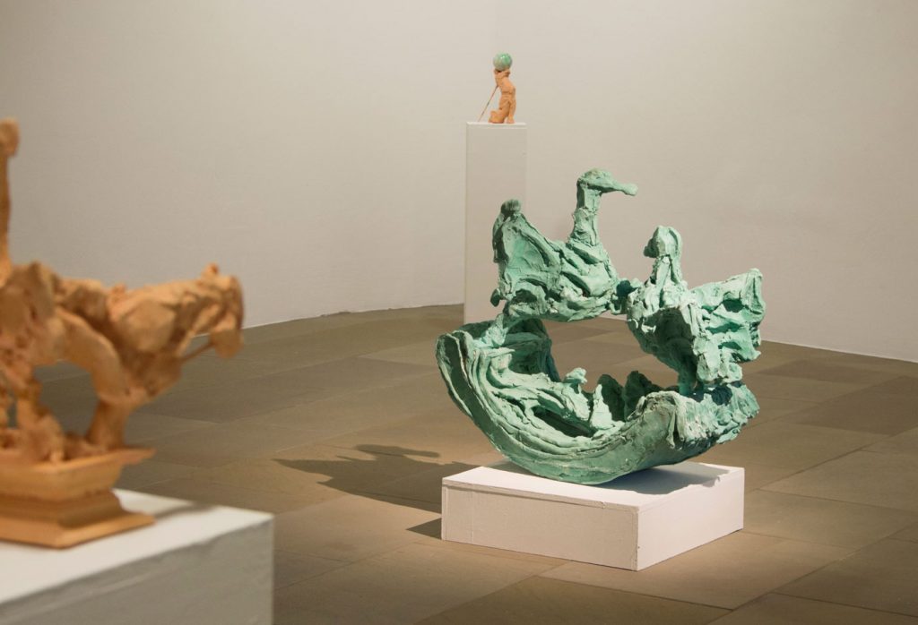 Exhibition view. 3 colourful sculptures can be seen in a darkened room.